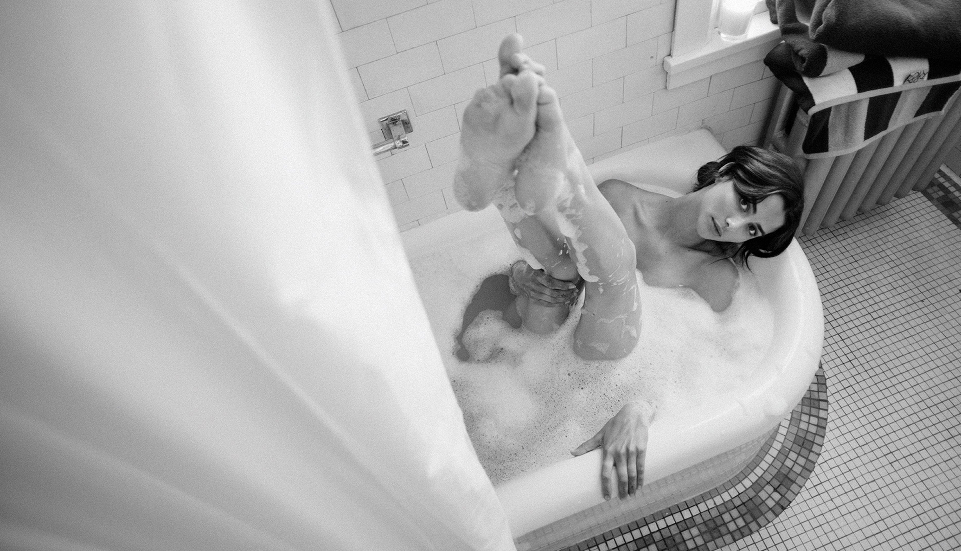 Person in a bathtub with bubbles, feet raised, in a tiled bathroom.