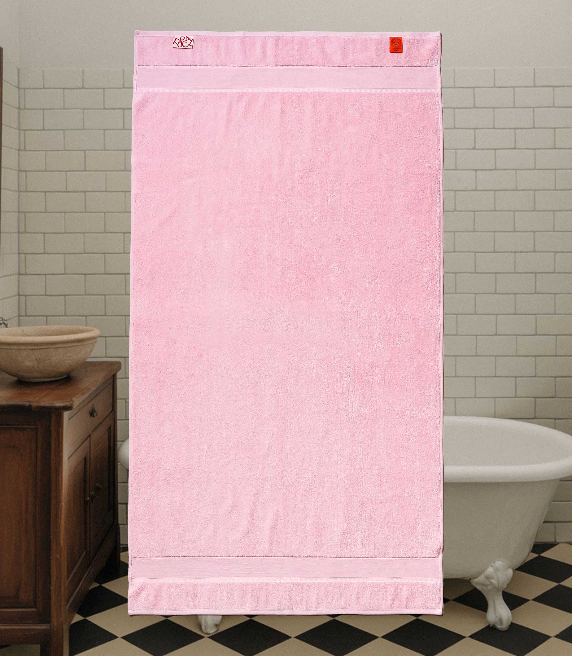 Pink towel hanging in a bathroom with tiled walls and a black and white checkered floor.